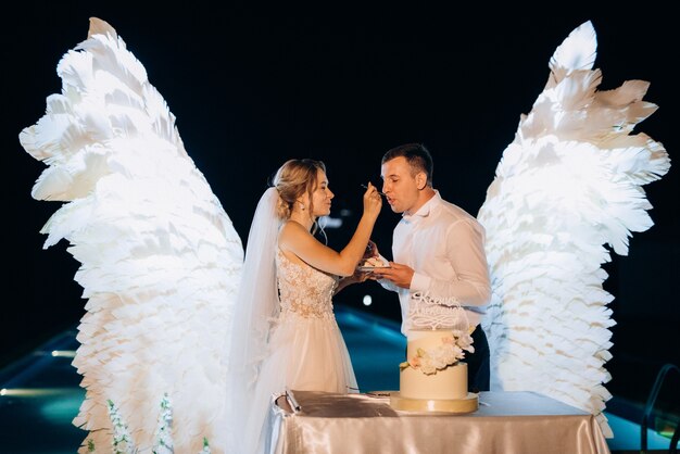 Les jeunes mariés coupent, rient et goûtent joyeusement le gâteau de mariage