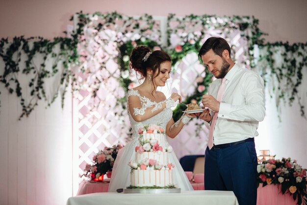 Les jeunes mariés coupent, rient et goûtent joyeusement le gâteau de mariage