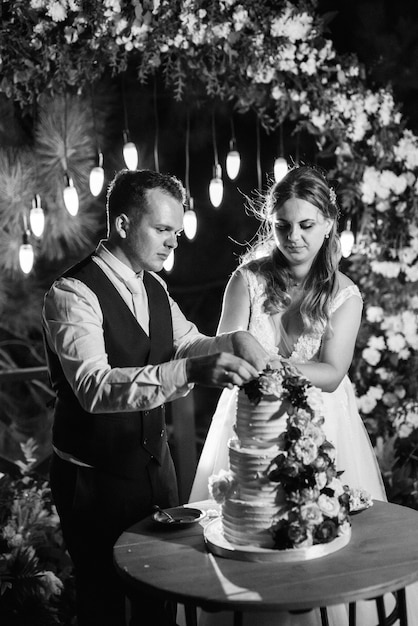 Les jeunes mariés coupent, rient et goûtent joyeusement le gâteau de mariage