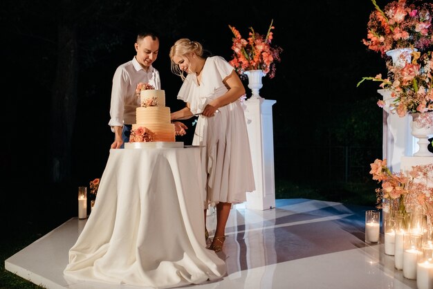 Les jeunes mariés coupent, rient et goûtent joyeusement le gâteau de mariage