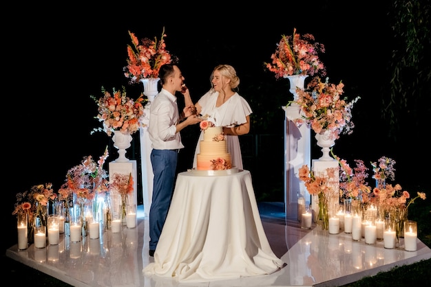 Les jeunes mariés coupent, rient et goûtent joyeusement le gâteau de mariage