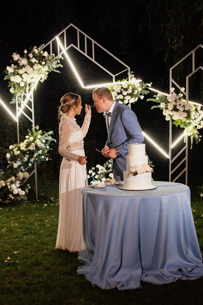 Les jeunes mariés coupent, rient et goûtent joyeusement le gâteau de mariage