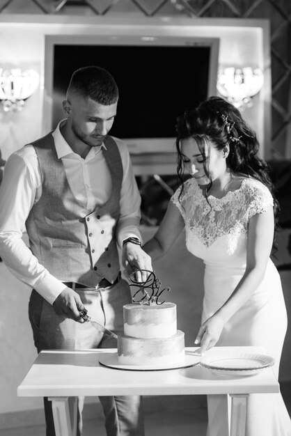 Les jeunes mariés coupent, rient et goûtent joyeusement le gâteau de mariage