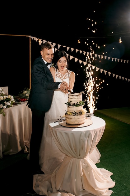 Les jeunes mariés coupent, rient et goûtent joyeusement le gâteau de mariage