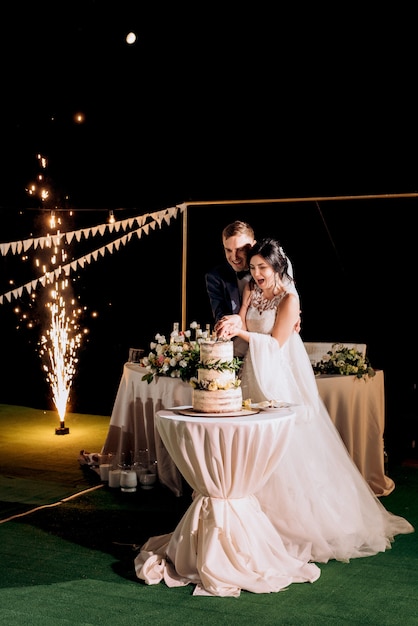 Les jeunes mariés coupent, rient et goûtent joyeusement le gâteau de mariage