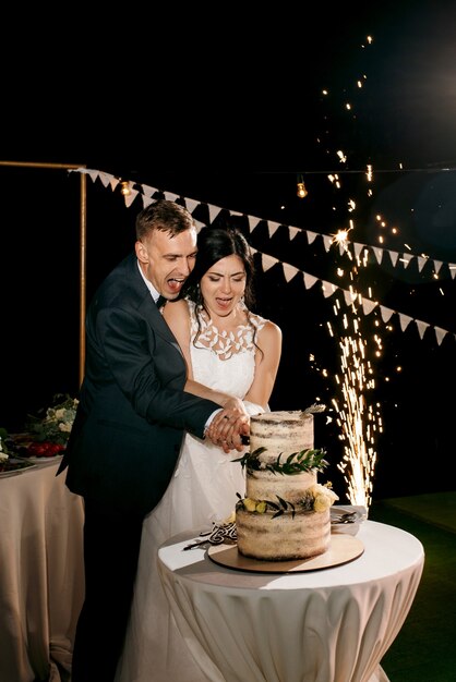 Les jeunes mariés coupent, rient et goûtent joyeusement le gâteau de mariage