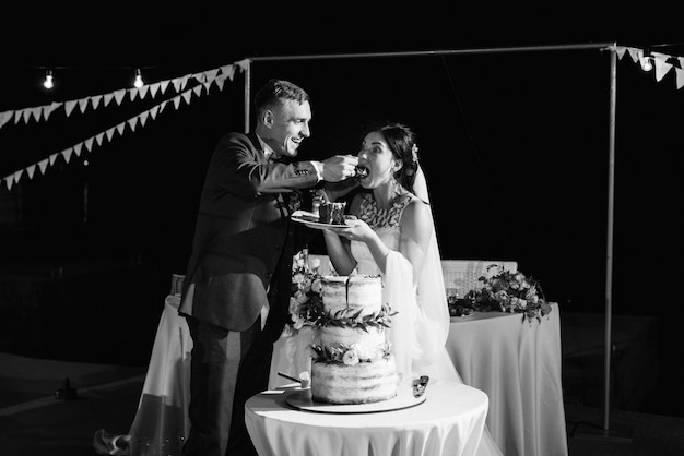 Les jeunes mariés coupent, rient et goûtent joyeusement le gâteau de mariage