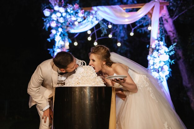 Les jeunes mariés coupent, rient et goûtent joyeusement le gâteau de mariage