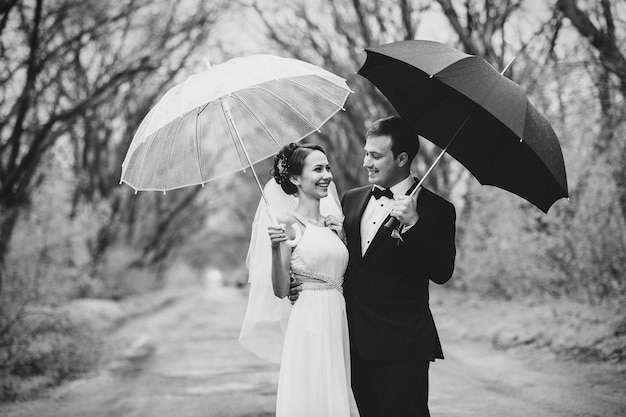 Jeunes mariés un jour de mariage pluvieux marchant sous un parapluie