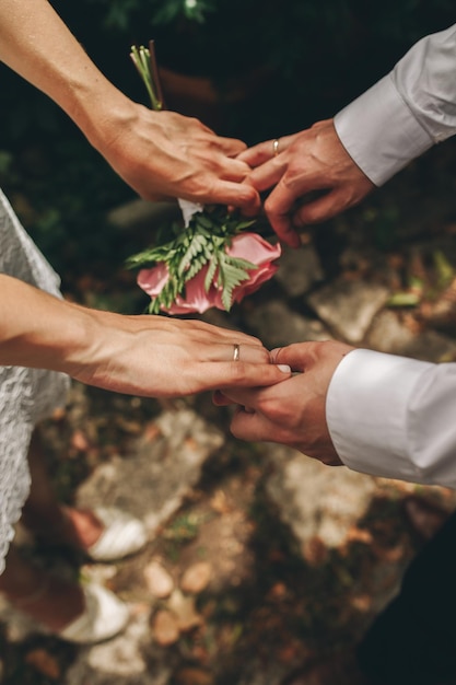 Photo les jeunes mariés avec leurs mains serrées avec leurs bagues de mariage et leur bouquet de roses