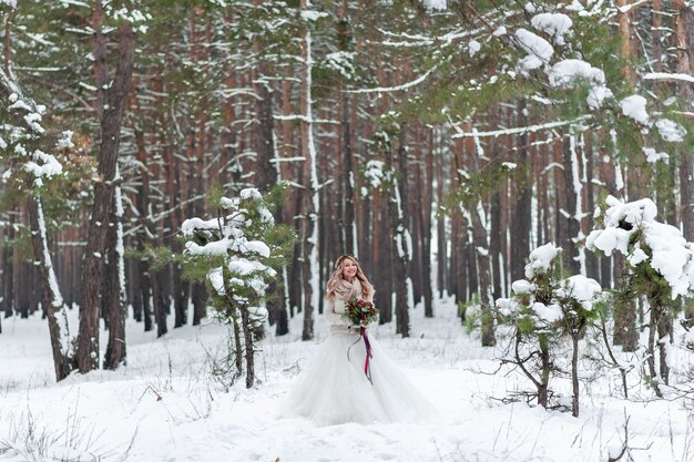 Jeunes mariés en pulls tricotés beiges dans la forêt enneigée. Les nouveaux mariés touchent le front. Mariage d'hiver. Espace copie