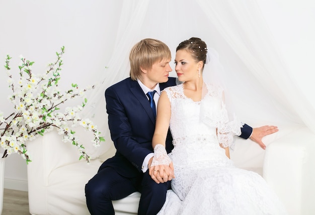 Jeunes mariés romantiques posant sur un canapé blanc de luxe