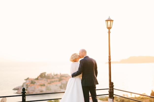 Les jeunes mariés s'embrassent sur une terrasse d'observation surplombant l'île de sveti stefan près de budva