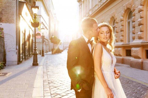 Jeunes mariés se serrant dans la rue de la vieille ville. Couple de mariage amoureux. Robe de luxe en strass.