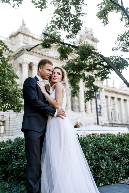 Jeunes mariés se serrant dans la rue de la vieille ville. Couple de mariage amoureux. Robe de luxe en strass.