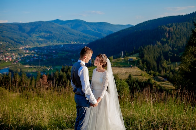 Les jeunes mariés se sourient et s'embrassent dans la prairie au sommet de la montagne. Promenade de mariage dans les bois à la montagne, les émotions douces du couple, photo pour la Saint Valentin