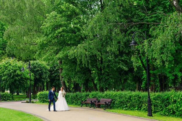 Les jeunes mariés se tiennent la main et marchent dans un magnifique parc. mariée tient un bouquet de mariage.