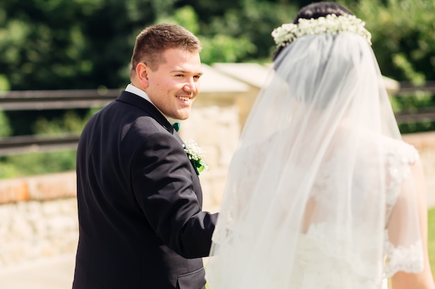 Les jeunes mariés se tiennent la main et se regardent Le marié en costume élégant sourit à la mariée