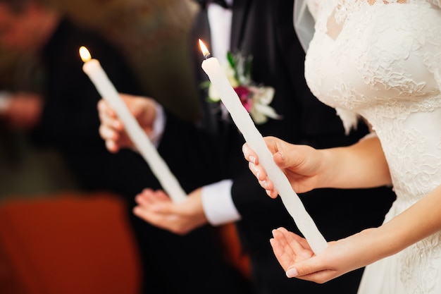 Les jeunes mariés tiennent des bougies sur les mains dans l'église