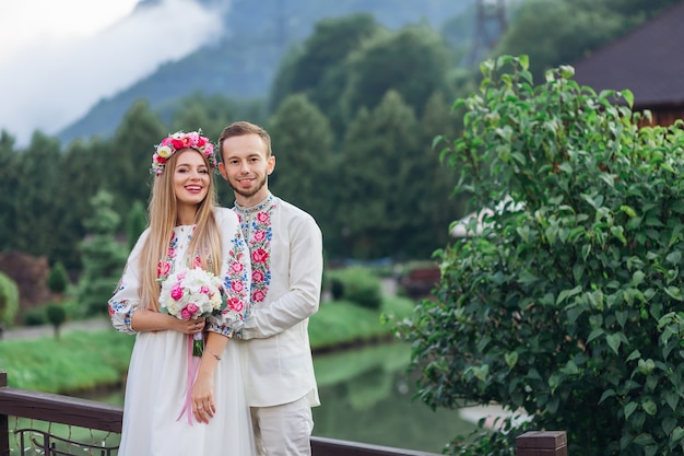 Les jeunes mariés en vêtements brodés souriant et regardant la caméra dans le contexte des montagnes et des lacs.