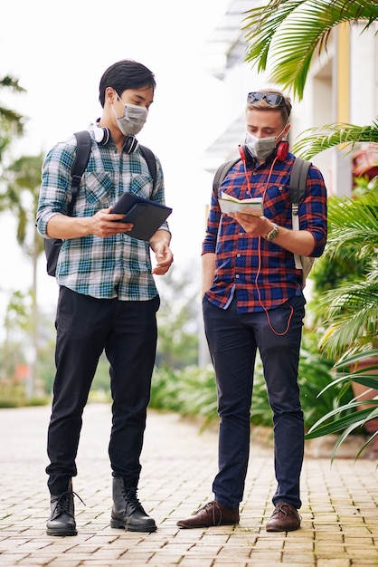 Jeunes en masques médicaux perdus dans la ville vérifiant une carte papier et une application de navigation en ligne