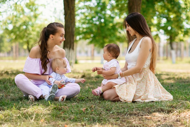 Les jeunes mères branchées et élégantes sont assis avec leurs filles sur l'herbe dans un parc.