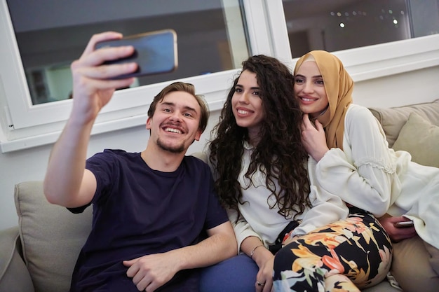 Jeunes musulmans heureux prenant le selfie dans la maison. Homme avec deux femmes passant du temps ensemble