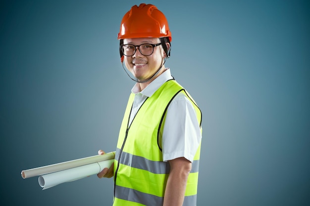 Jeunes ouvriers du bâtiment asiatiques dans un casque de sécurité et tenant les plans laminés isolés sur fond bleu