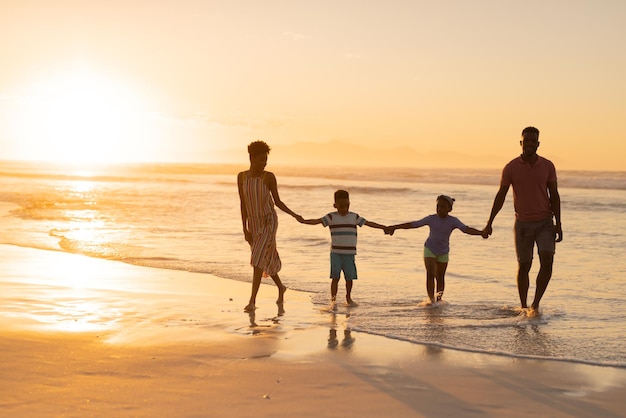 Jeunes parents afro-américains tenant les mains de leur fils et de leur fille tout en marchant sur le rivage contre le ciel