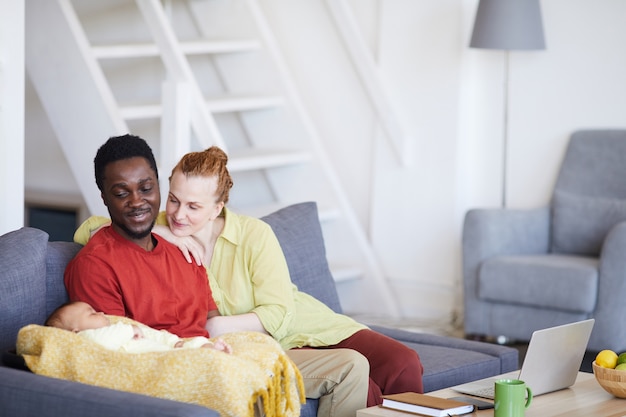 Jeunes parents assis sur un canapé et regardant leur bébé pendant qu'il dort, ils sont assis sur un canapé dans le salon