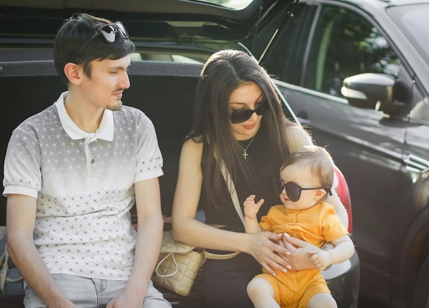 Les jeunes parents caucasiens tiennent dans leurs bras une petite fille dans ses bras assise dans le coffre ouvert