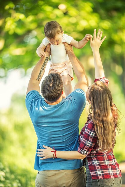 Photo des jeunes parents heureux jettent leur petite fille dans le parc.