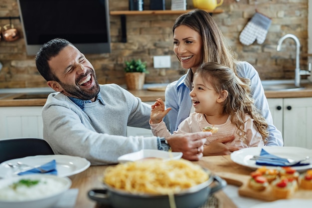 Jeunes parents heureux s'amusant avec leur petite fille pendant le déjeuner à table à manger