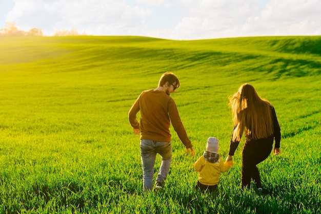 Jeunes parents avec un jeune fils marchant sur un champ au coucher du soleil en été. Concept de famille