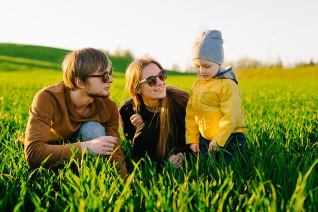 Jeunes parents avec un jeune fils marchant sur un champ au coucher du soleil en été. Concept de famille