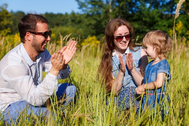 Les jeunes parents en lunettes de soleil frappent des mains avec leur petite fille souriante