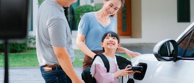 Jeunes parents progressistes et fille vivant dans une maison avec une voiture électrique