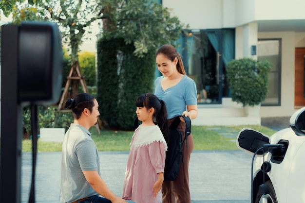 Jeunes parents progressistes et fille vivant dans une maison avec une voiture électrique