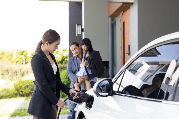 Jeunes parents progressistes et fille vivant dans une maison avec une voiture électrique