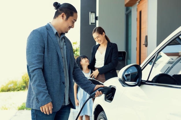 Jeunes parents progressistes et fille vivant dans une maison avec une voiture électrique