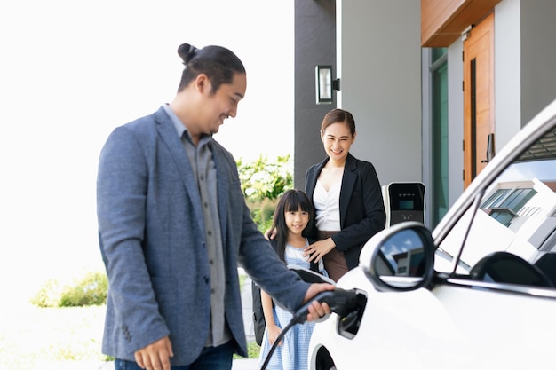 Jeunes parents progressistes et fille vivant dans une maison avec une voiture électrique