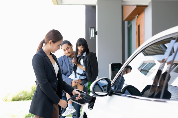 Jeunes parents progressistes et fille vivant dans une maison avec une voiture électrique