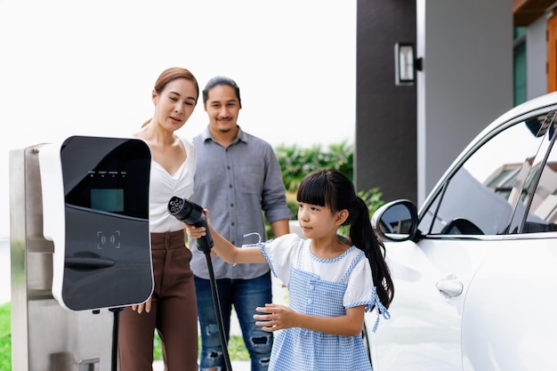 Jeunes parents progressistes et fille vivant dans une maison avec une voiture électrique