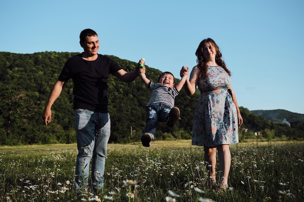 Les jeunes parents tiennent leur jeune fils à deux mains et le balancent d'avant en arrière