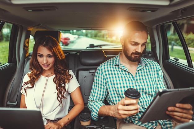 De jeunes partenaires commerciaux de confiance travaillent sur un voyage d'affaires sur le siège arrière de la voiture.