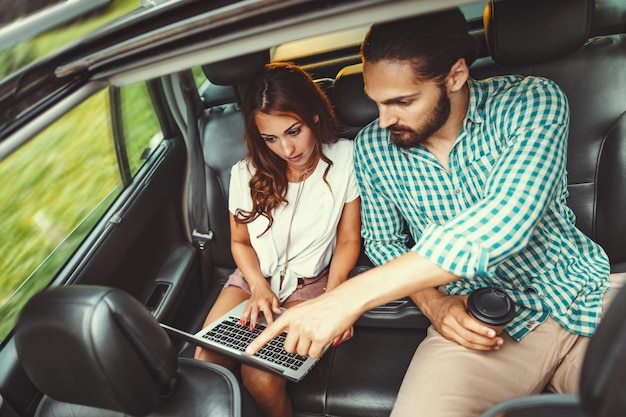 De jeunes partenaires commerciaux de confiance travaillent sur un voyage d'affaires sur le siège arrière de la voiture.