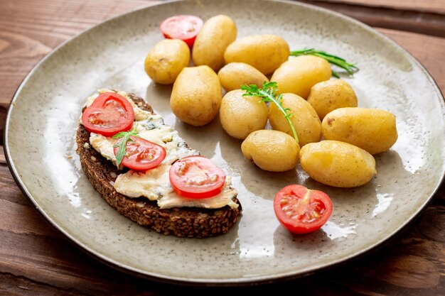 Jeunes pommes de terre bouillies et pain aux céréales avec fromage bleu et tomates sur une assiette sur un fond en bois. La nourriture végétarienne.