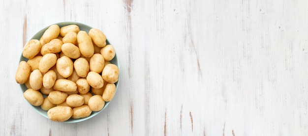 Jeunes pommes de terre crues petites sur une assiette sur un fond en bois blanc. Bannière. Place pour votre texte.