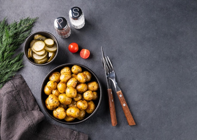 Jeunes pommes de terre fraîches rôties dans une poêle noire avec tomates et herbes sur fond sombre