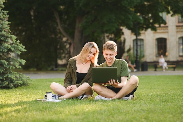 Jeunes positifs étudiant avec un ordinateur portable en pause dans la pelouse du parc